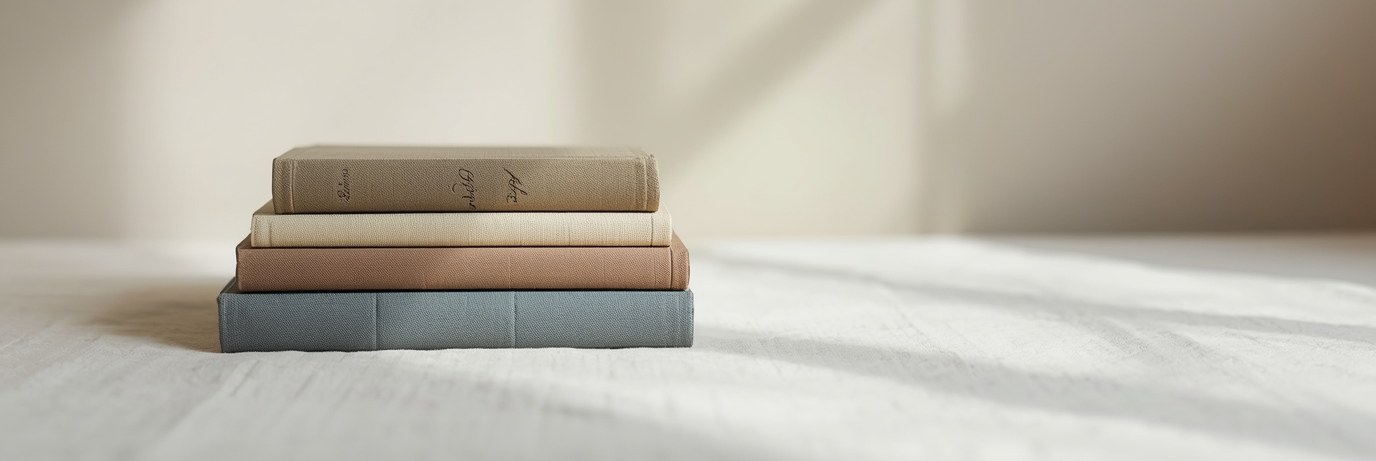 A small quiet stack of old cloth-bound books, one with a slate-blue spine, on cream linen in soft light